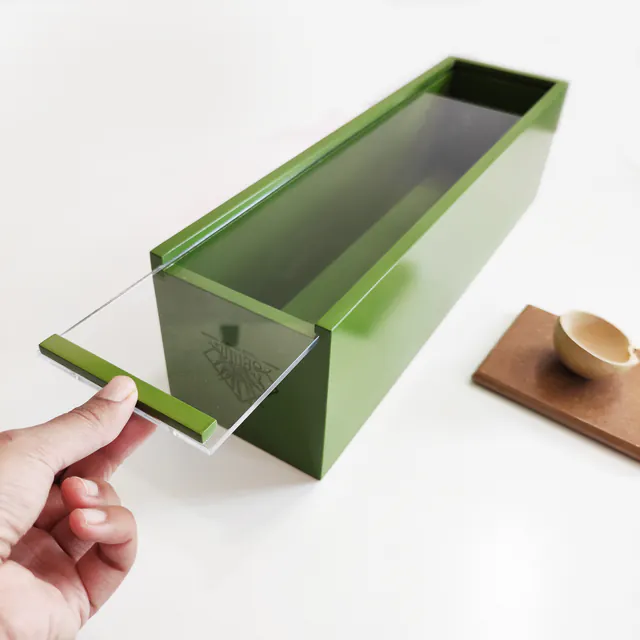 Caja verde alargada con la tapa transparente deslizada hacia afuera, sostenida con una mano