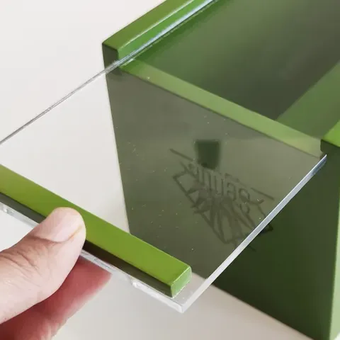 Tapa deslizable de acrílico transparente sostenida con la mano, sobre una caja laqueada en verde hecha para Sentir